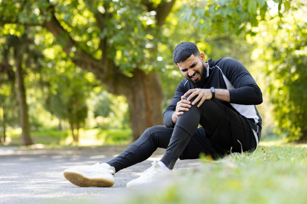 male athlete holds his knee pain feeling discomfort fitness session sunny park